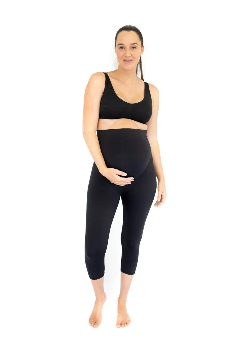 Woman smiling while doing a workout at home wearing black Emamaco maternity nursing crop top and leggings.