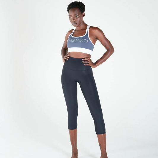 Woman wearing black postpartum recovery shorts with deep pockets, standing in a relaxed bedroom setting.