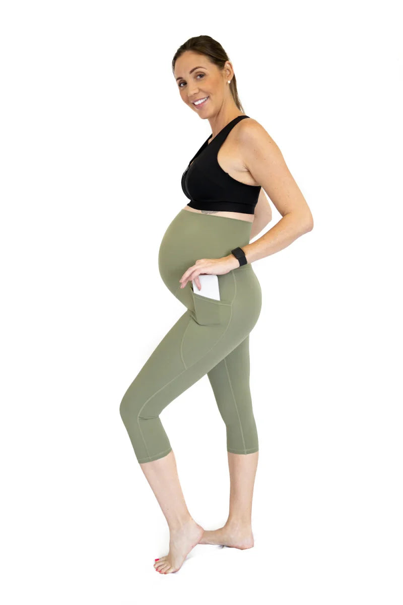 Pregnant woman in black top and olive green maternity leggings with pockets for comfort