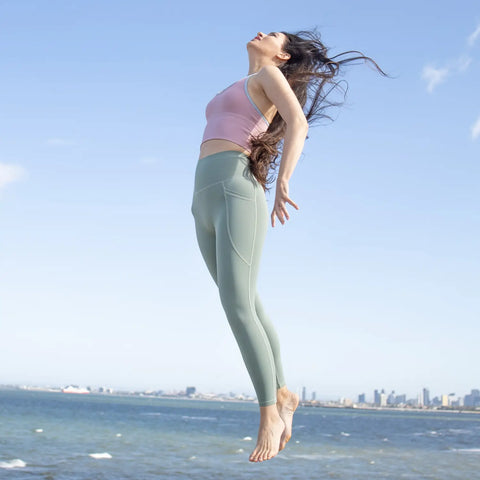 Person in mint green leggings and pink top jumping by the seaside to stay active.