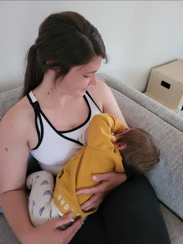 Parent in a white tank nursing a baby in a yellow blanket, highlighting nursing sports needs.