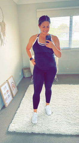 Angela Reakes in purple activewear and white sneakers taking a mirror selfie.
