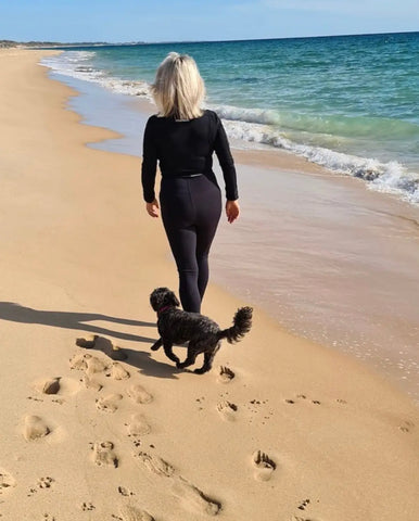 Person in black activewear walking dark fluffy dog on the shoreline at Emamaco.